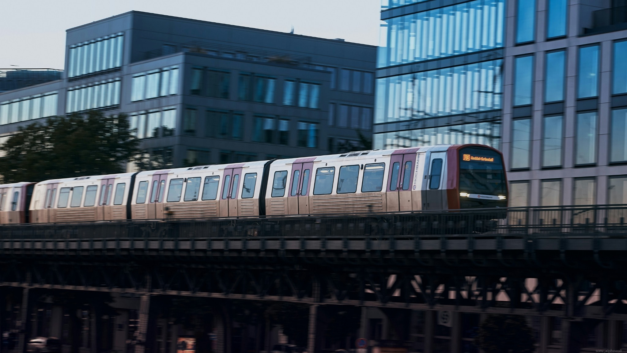 Hamburger U-Bahn auf einer Hochbahnbrücke vor moderner Glasarchitektur – Foto von Julio Wolf